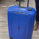Dame som jobber i butikk og demonstrerer en Samsonite Essens koffert i en dyp blå farge. Hun står i en butikk og har andre kofferter og vesker i bakgrunnen.