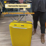 dame som jobber i butikk og demonstrerer en gul Samsonite Upscape koffert. I bakgrunnen er det kofferter i ulike størrelser, fasonger og farger plassert i hyller.