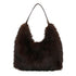 A plush dark brown foxtail handbag made of faux fur with slender black leather handles in hobo style