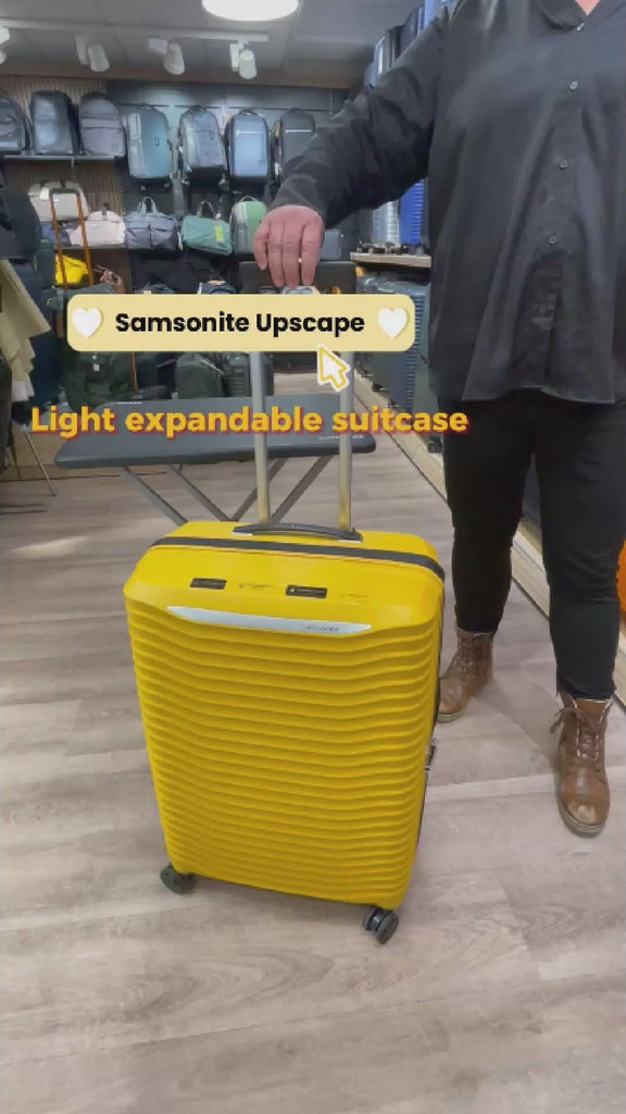 dame som jobber i butikk og demonstrerer en gul Samsonite Upscape koffert. I bakgrunnen er det kofferter i ulike størrelser, fasonger og farger plassert i hyller. 